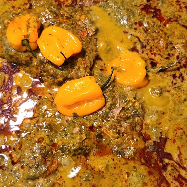 Close-up of a vibrant Senegalese dish with green sauce, red oil, and four bright yellow habanero peppers.