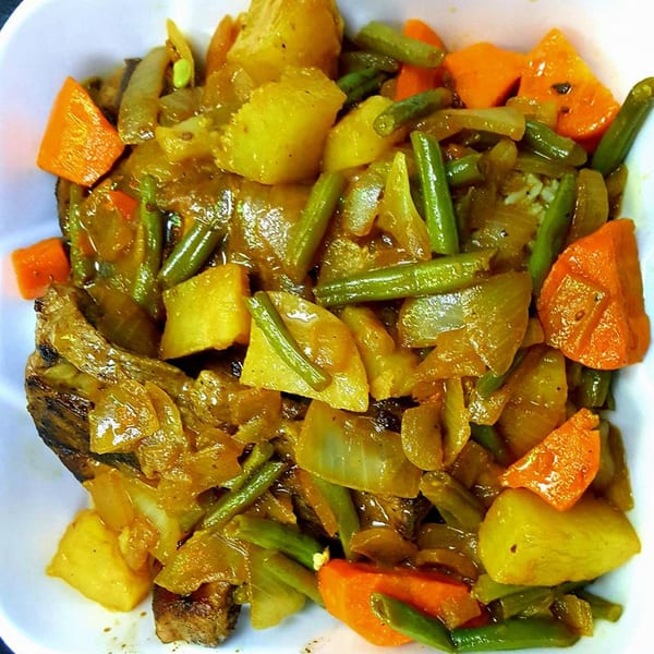 Close-up of a Senegalese dish with meat, potatoes, green beans, carrots, and onions in a rich sauce.
