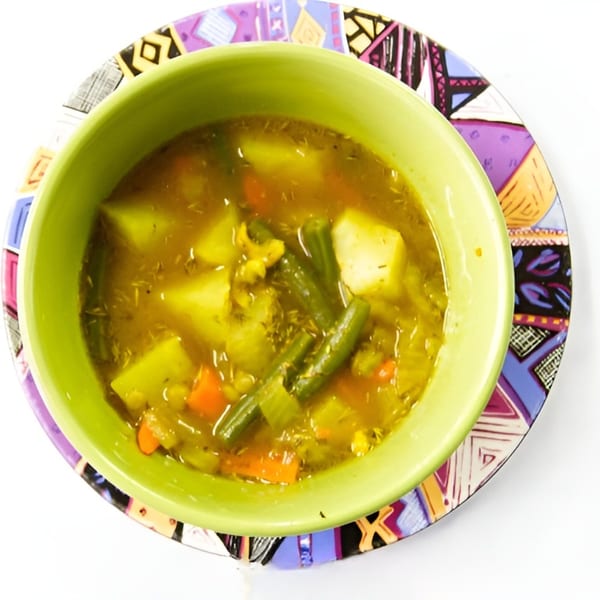 A vibrant green bowl of Badou Senegalese vegetable soup with potatoes, carrots, and green beans.