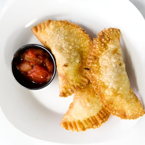 Three golden-fried Senegalese empanadas with a side of red salsa on a white plate.
