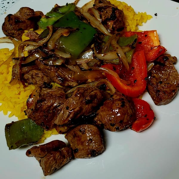 Senegalese beef dibi with yellow rice, grilled onions, and bell peppers on a white plate.